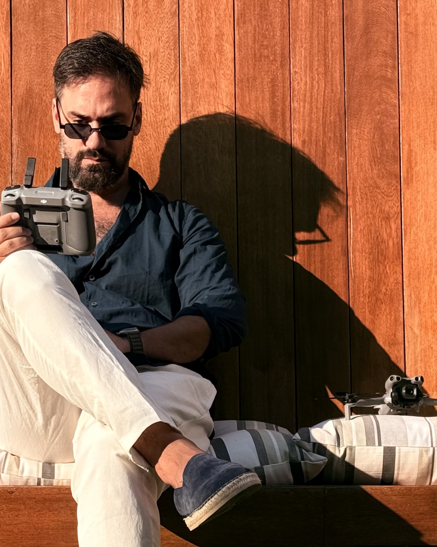 Marc sentado contra una pared de madera, con el mando del dron en las manos y el aparato posado a su lado