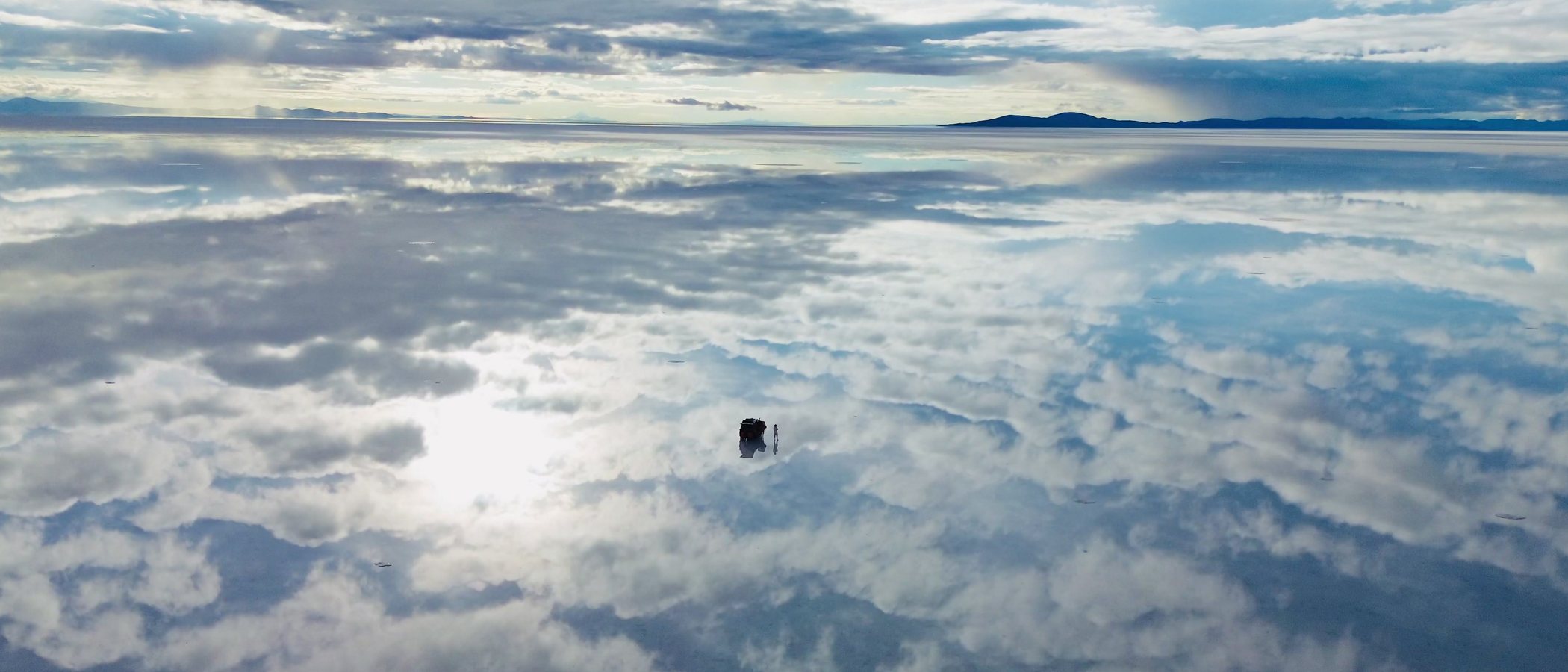 Un vehículo solo sobre el salar de Uyuni inundado, con las nubes reflejadas