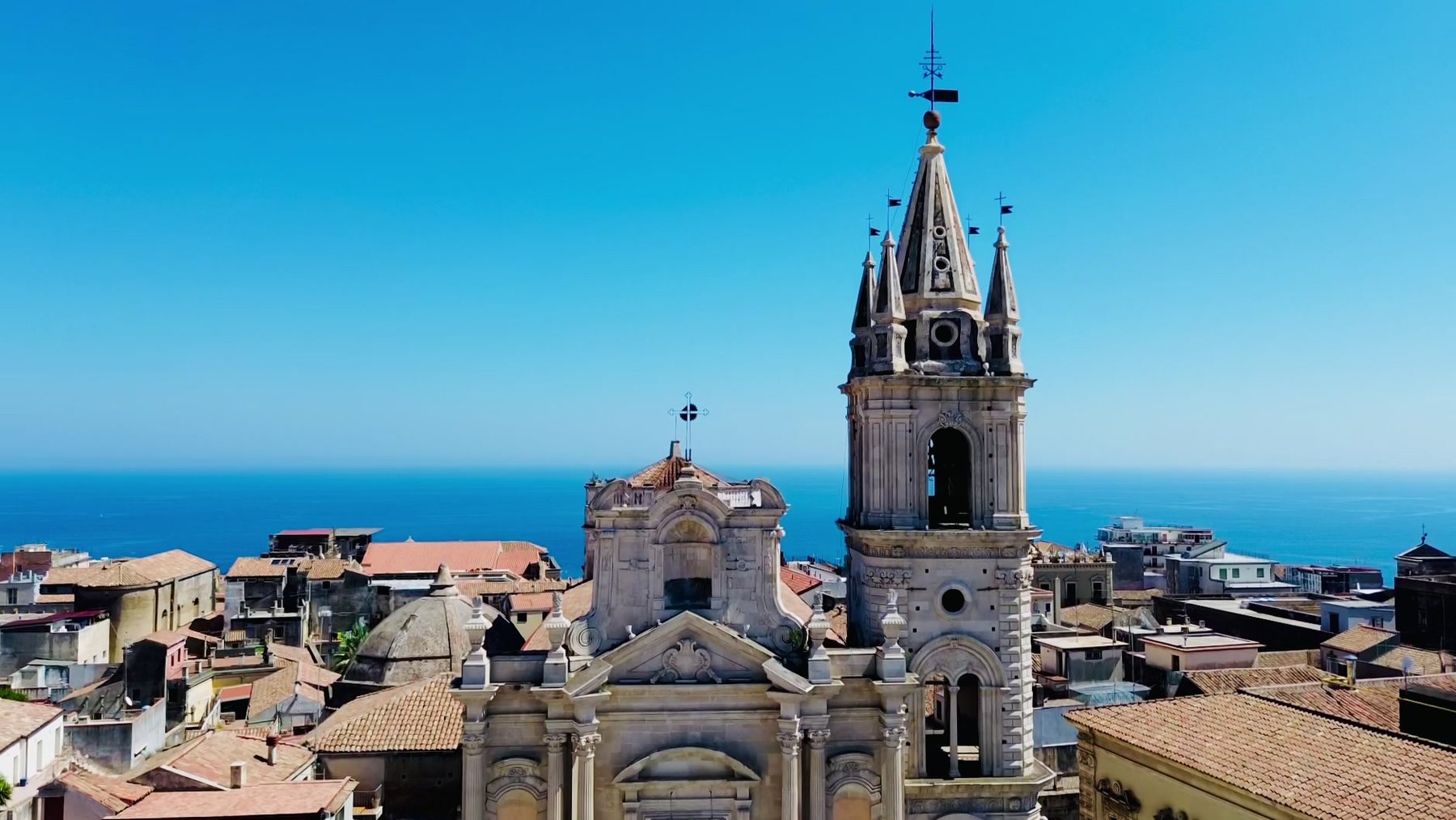 Iglesia con dos campanarios sobre un pueblo siciliano y el mar al fondo