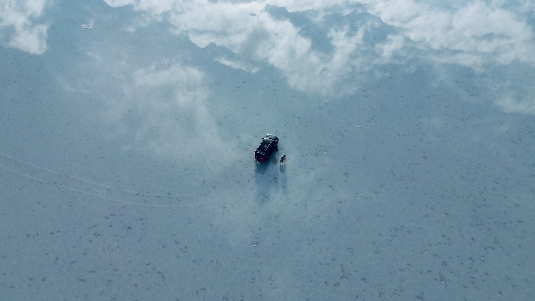Cenital de un todoterreno sobre el salar con las nubes reflejadas
