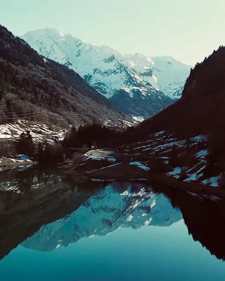 Valle alpino nevado reflejado en la superficie quieta de un lago
