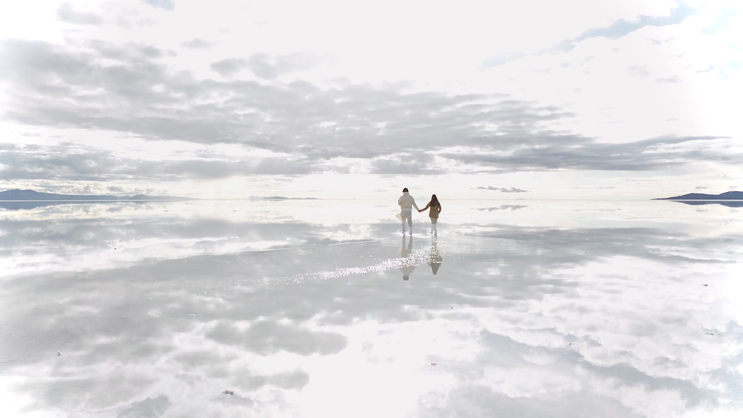 Dos figuras cruzando el salar de Uyuni inundado, que refleja el cielo